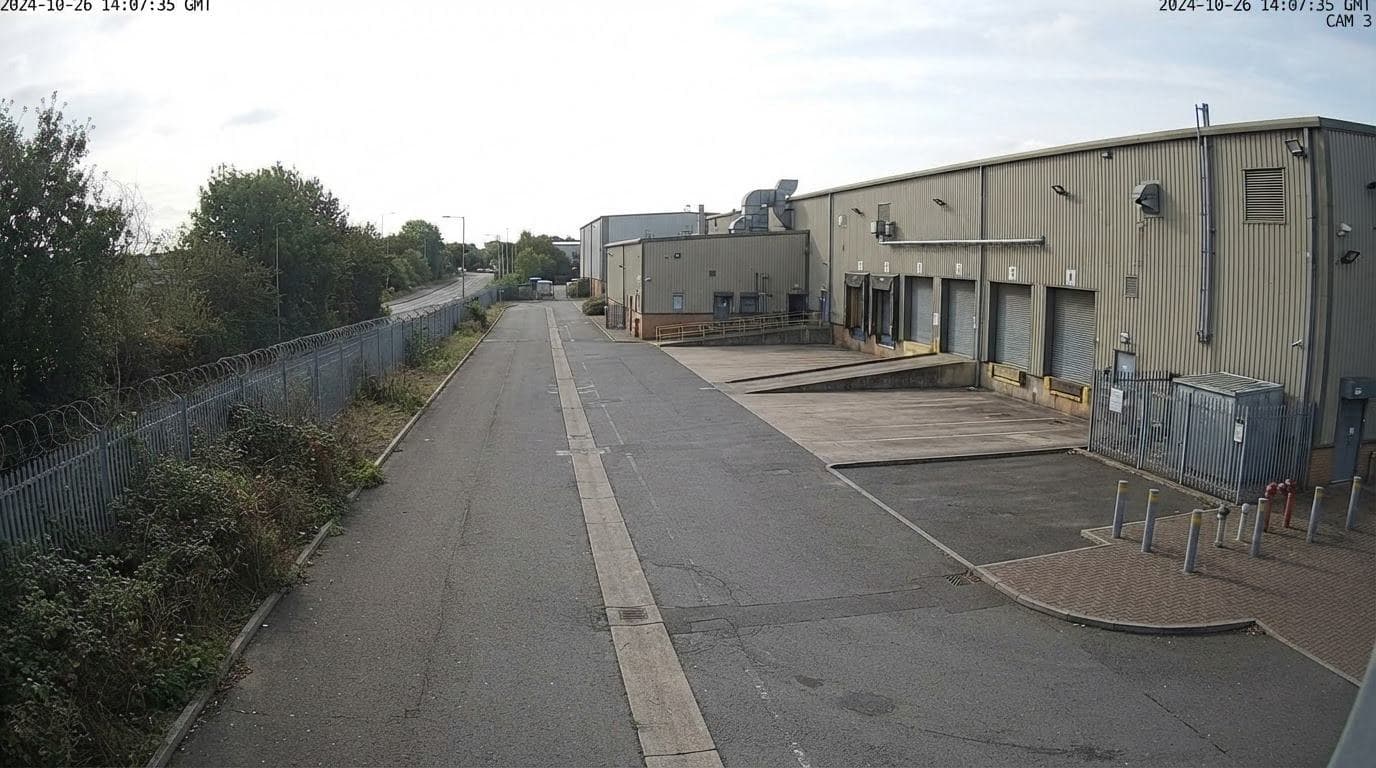 An empty service road beside a warehouse, seen by a wide-angle camera